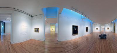 Panorama of a white walled gallery space, with various paintings in ornate frames hung on the wall. In the center of the gallery is a modern, gray chair with 3 seats.