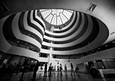 Multi-storied interior lobby of a modern art building. The lobby is open to the ornate windowed ceiling, and each of the floors is visible in the center of room in a spiral leading up to the ceiling.