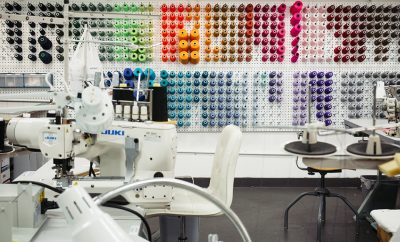 Sewing studio with machine workstations, and a wall of multiple colors of thread in the background.