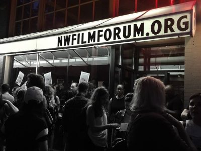Group of theater goers queue outside the entrance to a theater, the marquee out from reading "NWFILMFORUM.ORG"