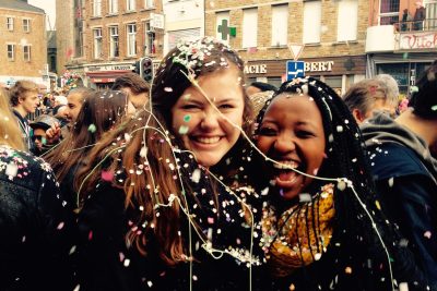 Two smiling youths in the middle of a street fair laugh and smile as they are covered in confetti and silly string