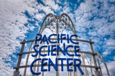 Decorative arch ways against a bright blue sky, with a sign in front reading "Pacific Science Center"
