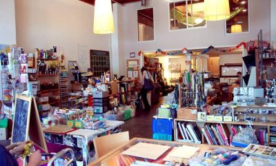Used art supply store with shelves full of crafting and art supplies, a few people browsing.