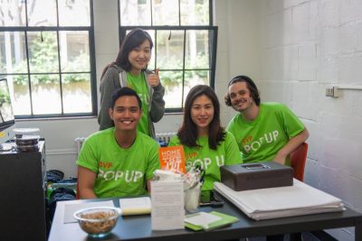 Students sit at a table wearing matching green tshirts that read "SVP Pop Up"