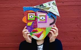 Person standing in front of a red bricked wall holds up an abstract face mask.
