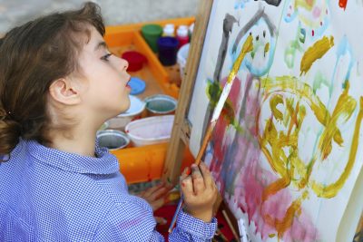 Child holding a paintbrush paints at an easel