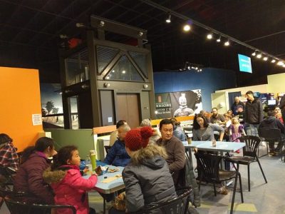 Interior of a museum cafe where several families and groups of people eat together.