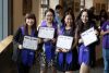 Group of smiling students posing with certificates and purple graduation sashes