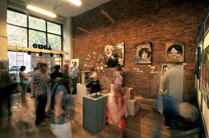 Interior of an art gallery with artwork displayed on pedestals and the wall. People chat and look at art in the space.