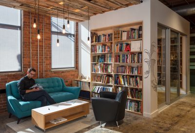 Person sits on a blue couch reading a book in a bright open office space