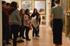 Group of students view work on an art gallery wall, while a docent stands in front of the group