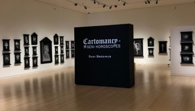 White walled gallery setting featuring black and white 2 dimensional artworks. A title wall reads "Cartomancy; Seni Horoscopes; Shay Bredimus" in the center.