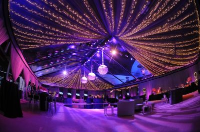 Dim and festive event space with a dance floor and casual seating. The ceiling is adorned with string lights and disco balls.