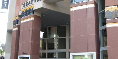 Entrance to modern art museum building with brown-red columns leading to an archway. Stone lettering on front of building reads "Seattle Art Museum"