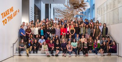 Group photo of Seattle Art Museum staff in museum lobby; some are seated on stairs and some are standing behind.