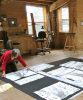 individual in an art studio space kneels on the floor, laying out a series of paintings on paper