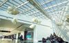 Interior of a brightly lit foyer in an airport, featuring abstract sculptural shapes hung from the ceiling and installed on the floor.