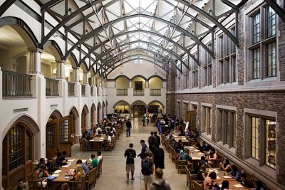 University hall with high ceilings and bright skylights, tables lining the sides with students studying.