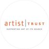 Grey circle outline, with orange and black text inside that reads, "artist trust in orange font. beneath that in smaller text reads: supporting art at its source"