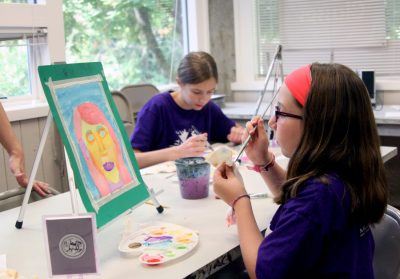 Two youths in matching purple shirts paint with watercolours in a brightly lit studio space.