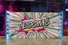 Large standing background panel with painted mural reading "Boom!" in an event space.