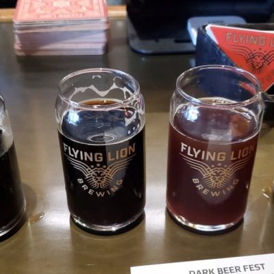 Two glasses of beer, with a logo and text that reads "Flying Lion Brewing"