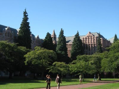 Exterior of red bricked university buildings, with students walking along the quad in the foreground.
