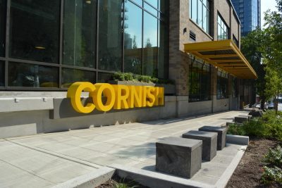 Brick and glass exterior of a college building, bright yellow letters out front reading "Cornish"