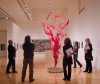 Group of people stand around a sculptural wire and red cloth art installation in a white walled gallery space