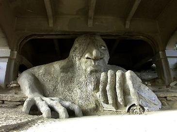 Concrete public art sculpture of a troll grabbing a car underneath bridge.