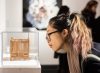 Young femme adult wearing glasses looks at an art object in a glass vitrine.