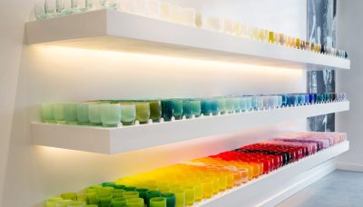 Different colored blown glass vessels displayed on a white wall shelf.