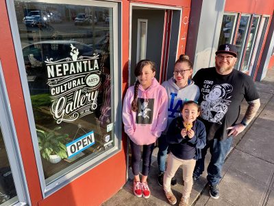 Family of four stands smiling in front of a bright red building, the window sign reading "Nepantla Art Gallery."