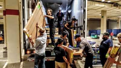 Group of people unload boxed artwork from a large moving truck.