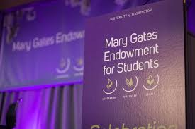 Purple panel board reads "Mary Gates Endowment for Students" in white text. In the background is a banner reading the same thing, hung on a purple curtained stage.