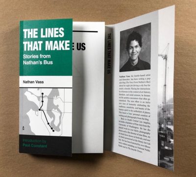 Book with cover featuring a black and white bus route map, the title in white text on green background reading "The Lines That Make Us; Stories from Nathans Bus." The inner flap is open to show an author photo, and biographic text.