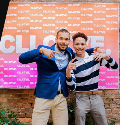 Two masc brown skinned people wearing business casual attire stand in front of a banner, the one on the left with their arm around the shoulders of the one on the right. The banner features a pink gradient background and the word "CLLCTVE" in white text repeated.