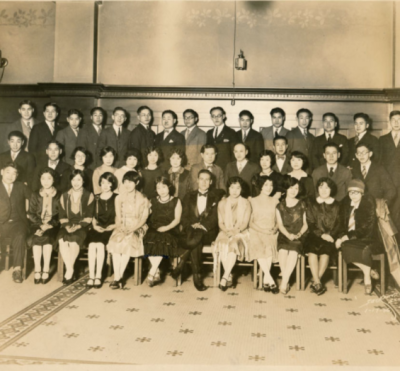 Black and white photograph of a group of a club of people, dressed in suits and dresses. The first row is seated, and the second and third rows stand behind the seated figures.