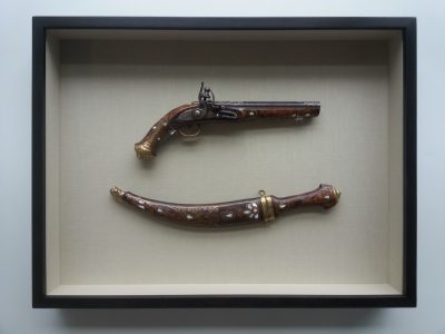 A black framed display box shows an antique, matching pistol and knife set, featuring wood inlay decorative elements.