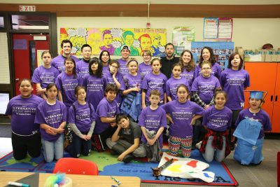 Group of school children and young adult mentors stand in a class room setting, all wearing matching purple tshirts that read "University of Washington; 2017 Alternative Spring Break; The Pipeline Project."