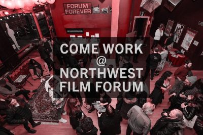 Transparent black text box with white text that reads "Come work @ Northwest Film Forum" overlaid across an image of a performance venue lobby full of people mingling and chatting.