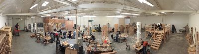 Panoramic view of a wood shop and fabrication studio. Several artists working on different woodworking and sculpture projects.