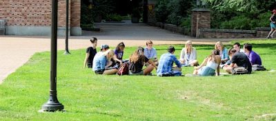 Group of students sit together on a green lawn on a University campus.