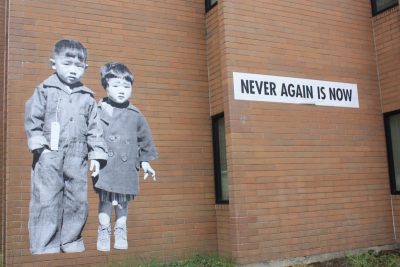 Wall mural on a red bricked building depicting two young children with Asian feature, and text to the right
