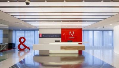 Brightly lit, minimal corporate office interior. Red sign at the end of the room reads "Adobe."
