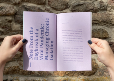 Person with painted nailed holds open a printed zine with pink pages and text.