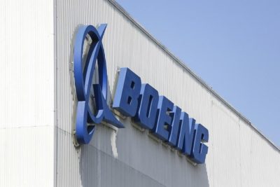Blue sign on the side of a white warehouse building that reads "Boeing"