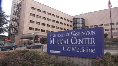 Beige hospital building behind a blue sign with white text reading "University of Washington Medical Center UW Medicine"
