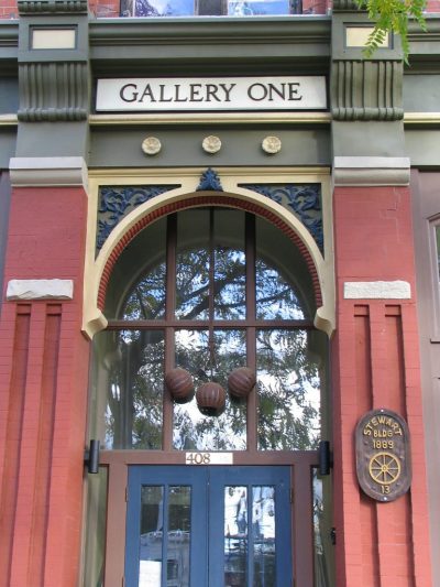 Front door entry to an exhibition and gallery space. An ornate stone archway over a glass windowed door. Sign above reads "Gallery One"