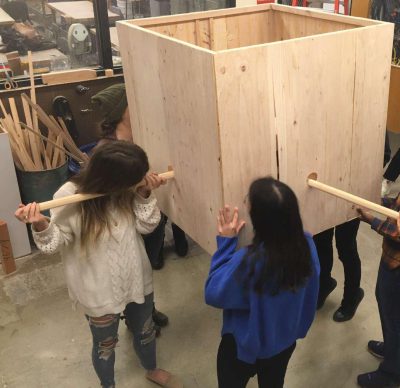 College students work together assembling a large square wooden box sculpture in a studio space